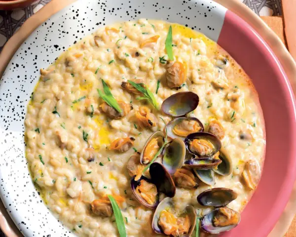 Un cremoso risotto alle vongole, guarnito con prezzemolo tritato e cozze fresche, servito in un piatto bianco a pois.