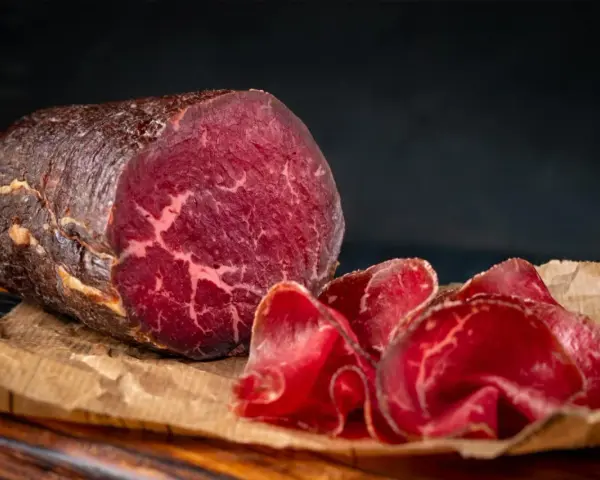 Un pezzo intero e fette sottili di bresaola, con la sua carne rossa e marezzata, evidenziano la differenza tra bresaola e punta d'anca.