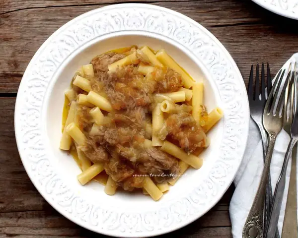 Piatto di pasta con ragù genovese napoletana, servito in un piatto bianco decorato, con forchette d'argento accanto.