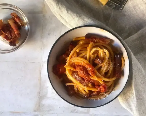 Un piatto invitante di bucatini all'amatriciana, con guanciale croccante e una salsa rossa saporita, spolverato di formaggio grattugiato.