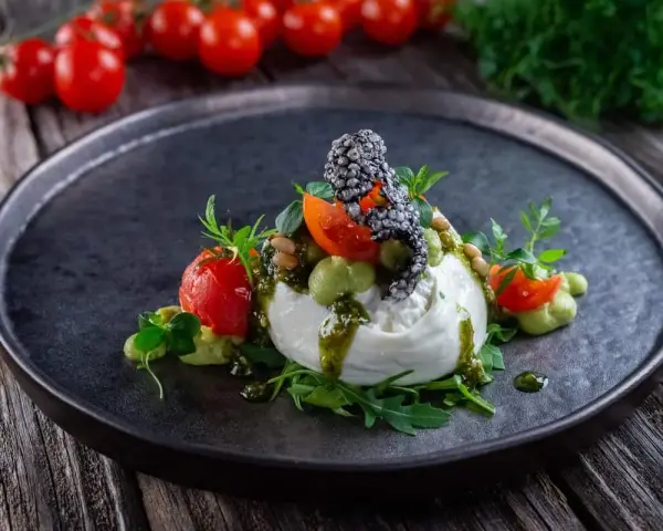 Burrata affumicata con pomodorini, crema di piselli, pinoli e pesto. Un piatto che esalta gli abbinamenti perfetti.