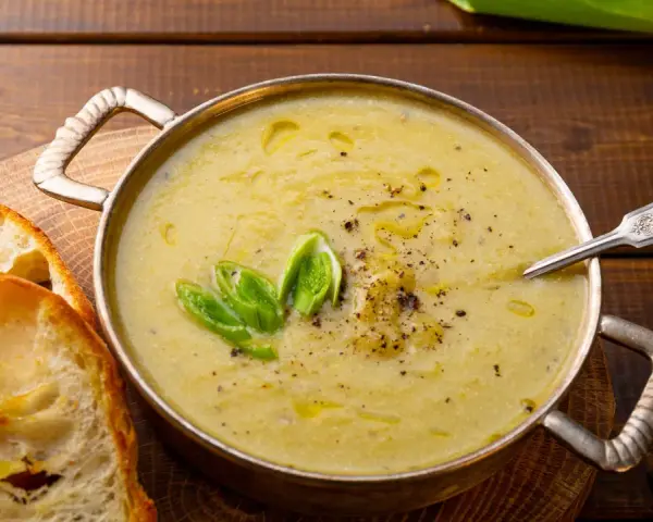 Una ciotola di calda crema di patate, guarnita con erba cipollina e pepe, servita con fette di pane tostato.