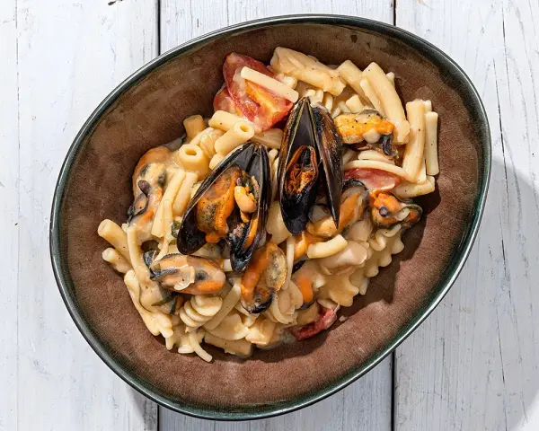 Piatto di pasta con fagioli e cozze, condita con pomodorini e una cremosa salsa.