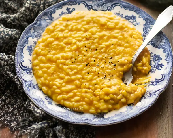 Un cremoso risotto con la zucca, servito su un piatto decorato con un motivo blu e bianco. Un cucchiaio d'argento è immerso nel piatto.