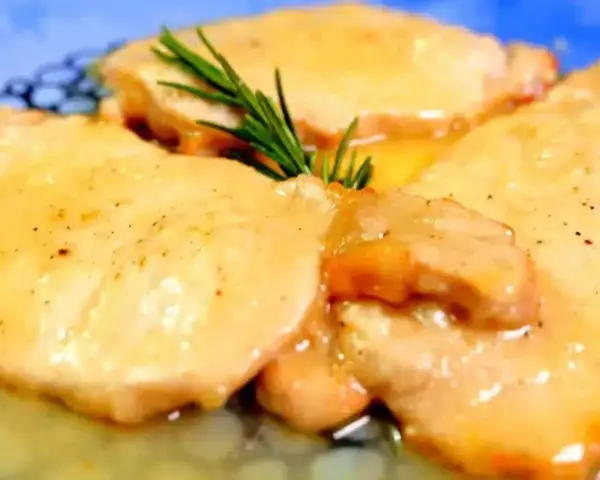 Deliziose scaloppine di maiale in salsa dorata, guarnite con un rametto di rosmarino fresco.