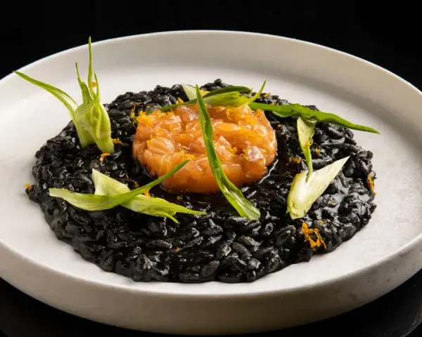 Un piatto di risotto al nero di seppia, guarnito con tartare di salmone e germogli verdi.