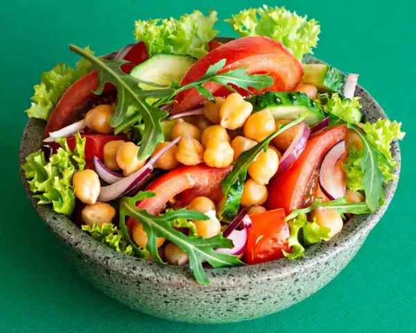 Insalata di ceci colorata con pomodori, cetrioli, cipolla rossa, lattuga e rucola in una ciotola grigia.