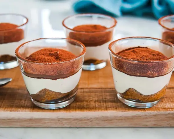Delizioso tiramisù con pavesini senza uova, servito in bicchierini trasparenti e spolverato di cacao.