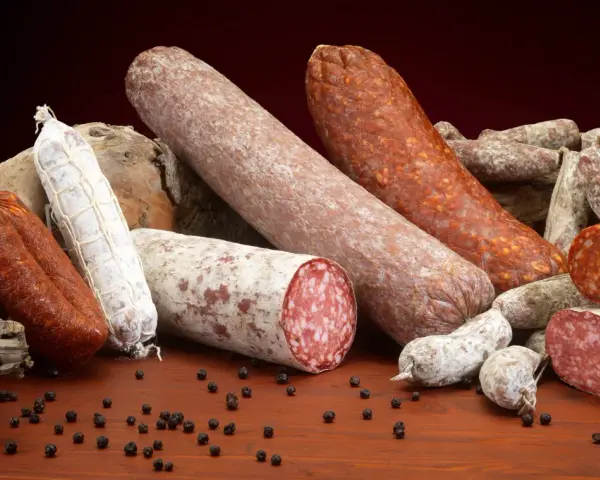 Un assortimento di salumi, tra cui spicca una grande fetta di carne insaccata, su un tavolo di legno con grani di pepe nero.
