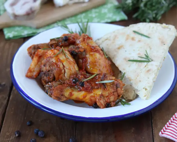 Piatto di friccò di pollo con pomodoro, olive e rosmarino, accompagnato da pane rustico.