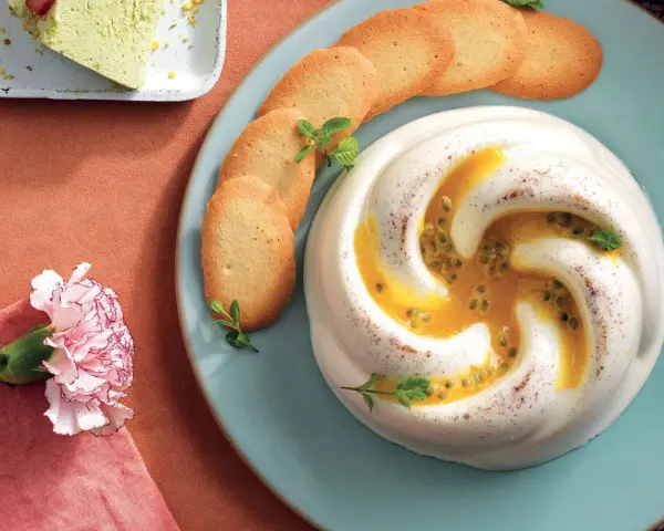 Dolce cremoso con cuore di frutto della passione, guarnito con biscotti e menta.