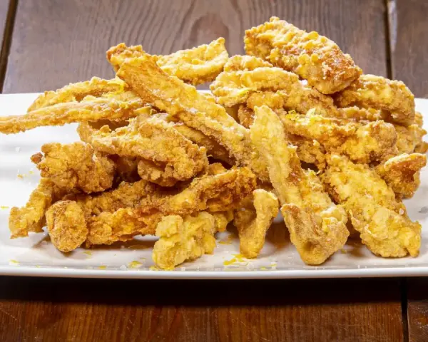 Un mucchio di croccante trippa fritta dorata, cosparsa di scorza di limone, su un piatto bianco.