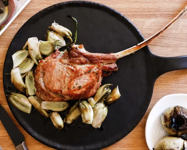 Un succulento tomahawk alla griglia, servito con verdure arrosto su un piatto nero.