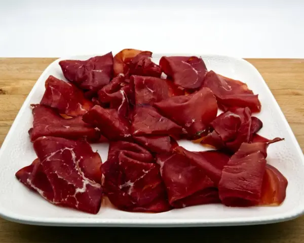 Fetta di bresaola scura, forse di cavallo, su un piatto bianco. Meglio bresaola di cavallo o manzo? La scelta è tua!