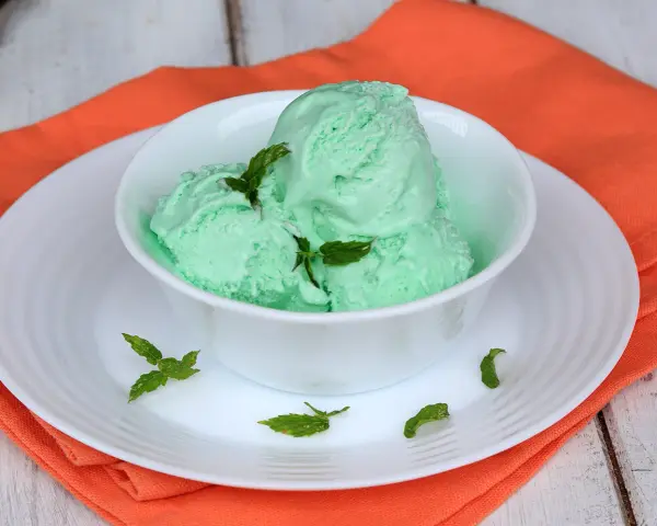 Coppa di cremoso gelato alla menta con latte condensato, guarnito con foglie di menta fresca.