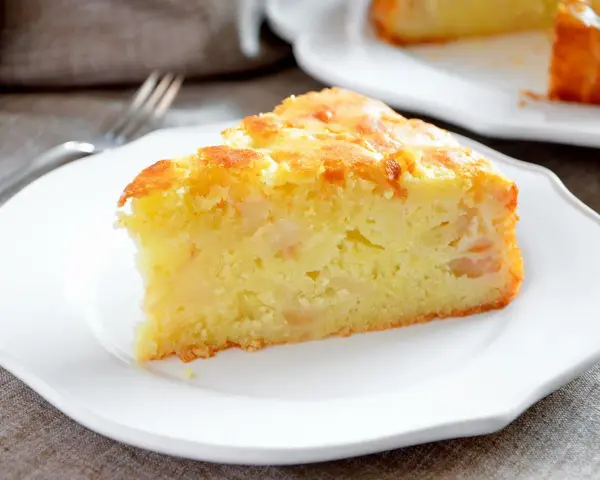 Una fetta di torta margherita con mele, soffice e dorata, servita su un piatto bianco.