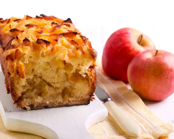 Torta con pandoro avanzato e mele, dorata e profumata, accanto a mele rosse fresche.