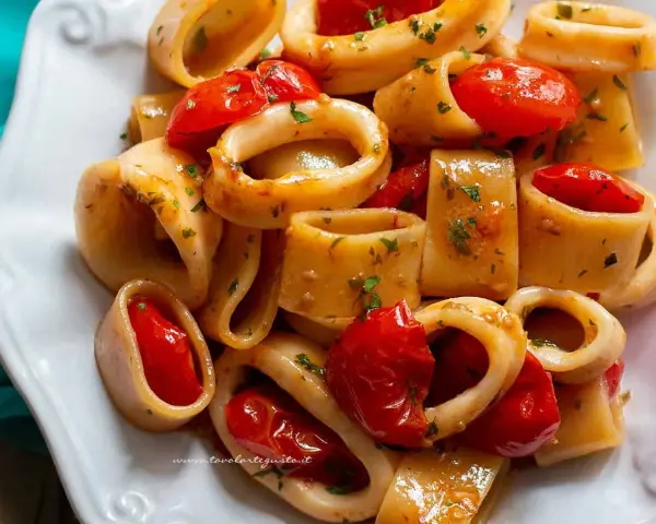 Un piatto invitante di pasta calamarata con pomodorini freschi e prezzemolo tritato, pronto per essere gustato.