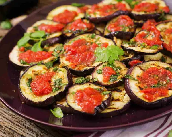 Fette di melanzane grigliate condite con salsa di pomodoro e basilico, un piatto gustoso di melanzane alla pizzaiola.