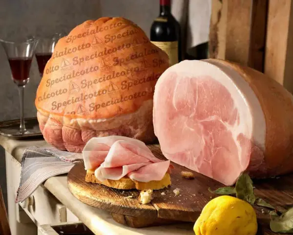 Due prosciutti, uno intero e uno affettato su pane, con una bottiglia di vino e un limone. Il cotto prosciutto è pronto per essere gustato.