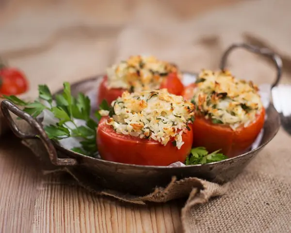 Pomodori ripieni di riso freddi, un piatto estivo gustoso e leggero, serviti in un vassoio rustico con prezzemolo fresco.