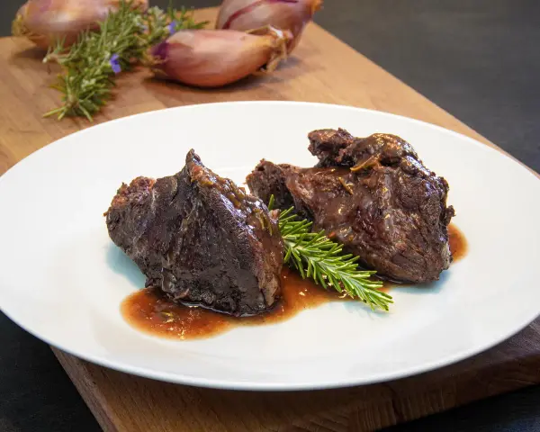 Guancia di manzo brasata, tenera e succulenta, servita su un piatto bianco con rosmarino fresco. Un piatto che fa chiedere: guancia di manzo cos'è?