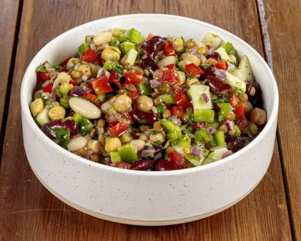 Una ciotola piena di colorata insalata di legumi, con ceci, fagioli, lenticchie, peperoni, cipolla rossa e prezzemolo fresco.