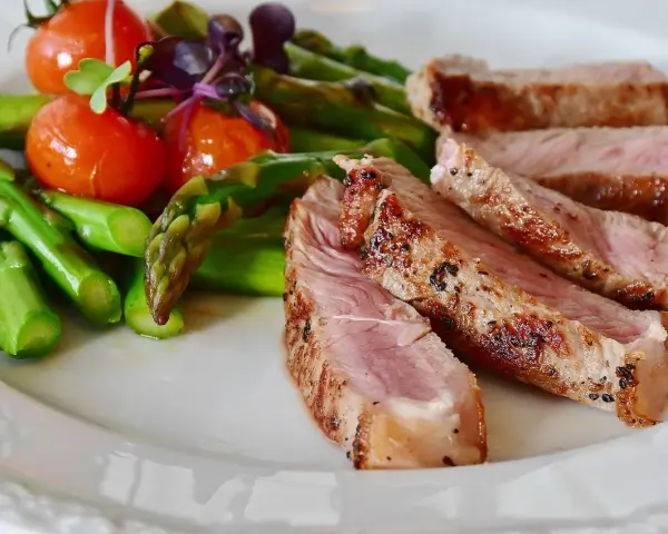 Fette di manzo magro cos'è? Succulenta carne con asparagi verdi e pomodorini su un piatto bianco.