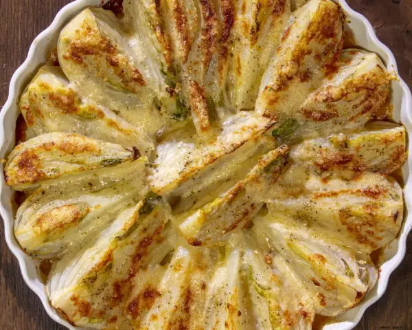 Finocchi al forno dorati e gratinati, serviti in una pirofila bianca su un tavolo di legno scuro.