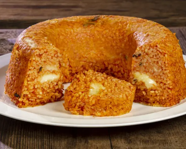 Un invitante timballo di riso, dorato e ripieno di formaggio filante, pronto per essere gustato su un piatto bianco.