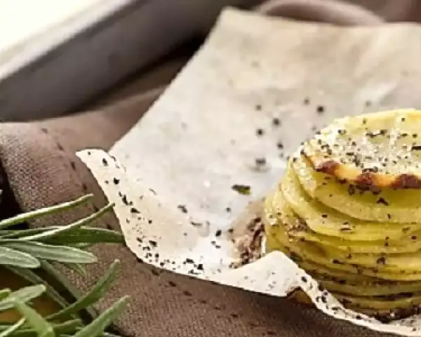 Deliziosa torretta di patate, sottili fette impilate e condite con erbe aromatiche e pepe nero, su carta da forno.