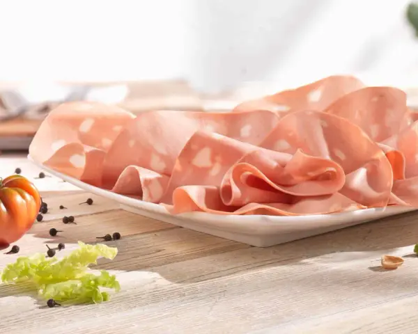 Fette di mortadella su piatto bianco, con pomodoro, lattuga e pepe. La differenza tra mortadella e bologna è nella qualità e negli ingredienti.