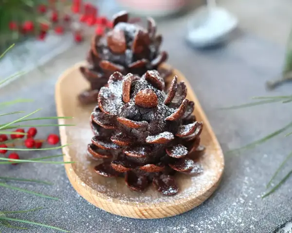 Deliziose pigne dolci decorate con zucchero a velo, su un vassoio di legno, con rami di pino e bacche rosse sullo sfondo.