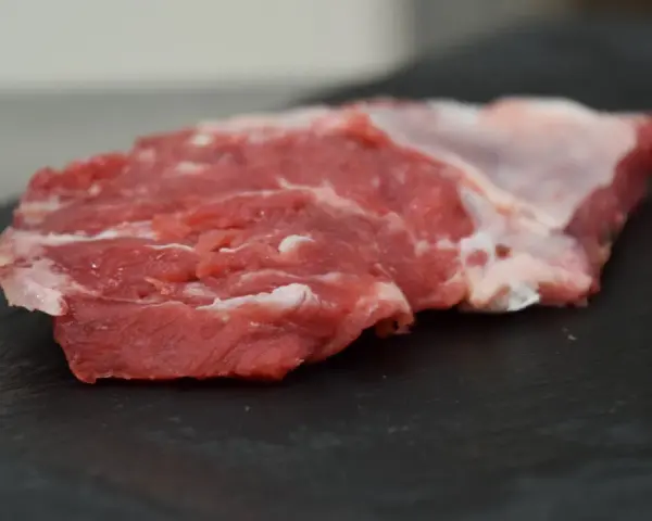 Un succulento spider steak crudo, con venature di grasso bianco, pronto per essere cucinato su una pietra scura.