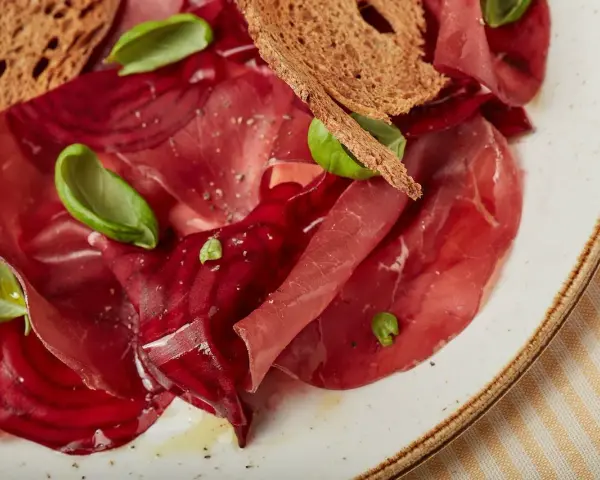 Fette di bresaola e barbabietola, esempi di salumi non insaccati quali sono, con crostini e basilico.