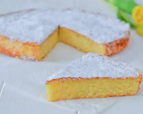 Una deliziosa torta caprese senza mandorle, spolverata di zucchero a velo, con una fetta tagliata.