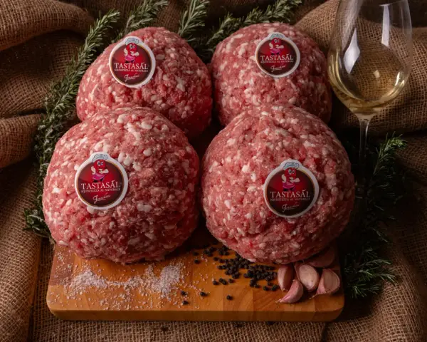Quattro sfere di carne macinata TASTASAL, con rosmarino, aglio, pepe e sale su un tagliere. Ingredienti freschi per un sapore autentico.