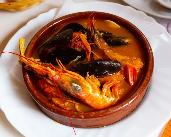 Una ricca zuppa di pesce in ciotola di terracotta, con gamberoni, cozze e pomodorini.