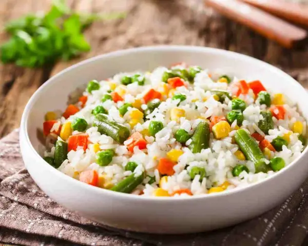 Un piatto di riso per insalata di riso, con piselli, carote, fagiolini e mais, su un tovagliolo di stoffa marrone.