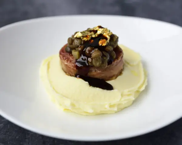 Piatto moderno con lenticchie e cotechino, un omaggio alla tradizione, servito su purè di patate e decorato con oro edule.