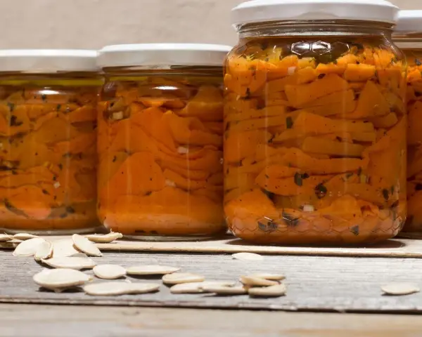Barattoli di zucca sott'olio in agrodolce, con semi di zucca sparsi sul tavolo di legno.
