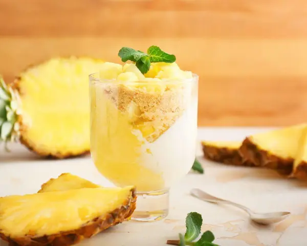 Delizioso dolce con ananas fresco, yogurt e crumble. Un bicchiere pieno di gusto tropicale, con fette di ananas e menta a guarnire.