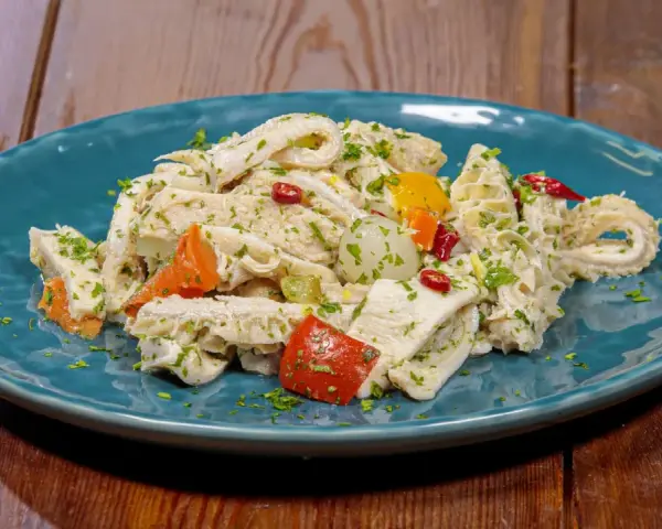 Piatto di insalata di trippa condita con erbe aromatiche, peperoncino e verdure colorate.