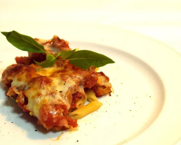 Porzione di pasta ncasciata fumante, con formaggio filante e basilico fresco, su un piatto bianco.