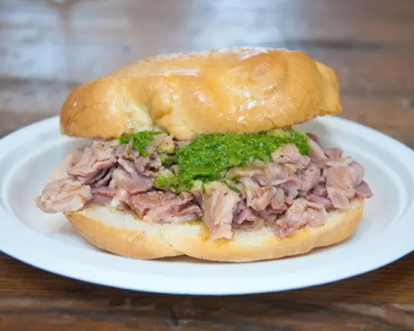 Panino con lampredotto, un classico street food fiorentino. La ricetta prevede trippa di bovino cotta e servita in un panino morbido con salsa verde.