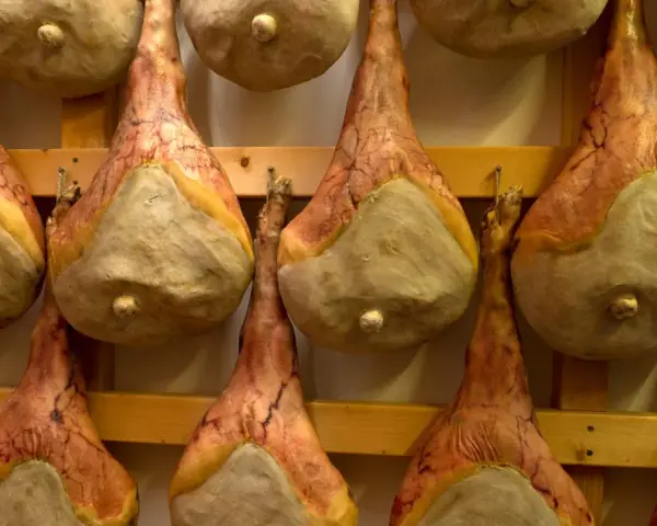 Filetti di salumi appesi a stagionare su scaffali di legno.