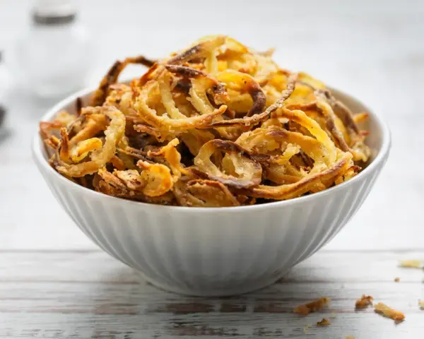 Ciotola piena di croccanti cipolle fritte dorate, perfette per accompagnare ogni piatto.