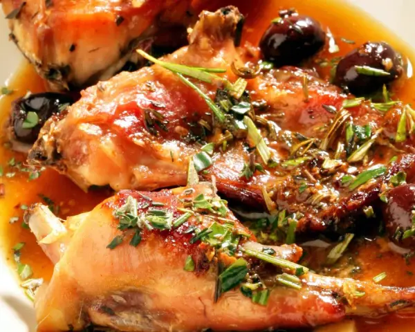Coniglio alla ligure succulento, con olive nere e erbe aromatiche, immerso in un sugo dorato.