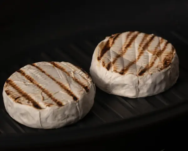 Due forme di formaggio da fare alla piastra, con belle striature dorate, cuociono in una padella scura.