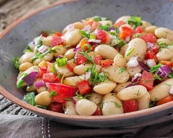 Insalata di fagioli bianchi, pomodori freschi, cipolla rossa e erbe aromatiche in una ciotola rustica. Un piatto colorato e salutare.